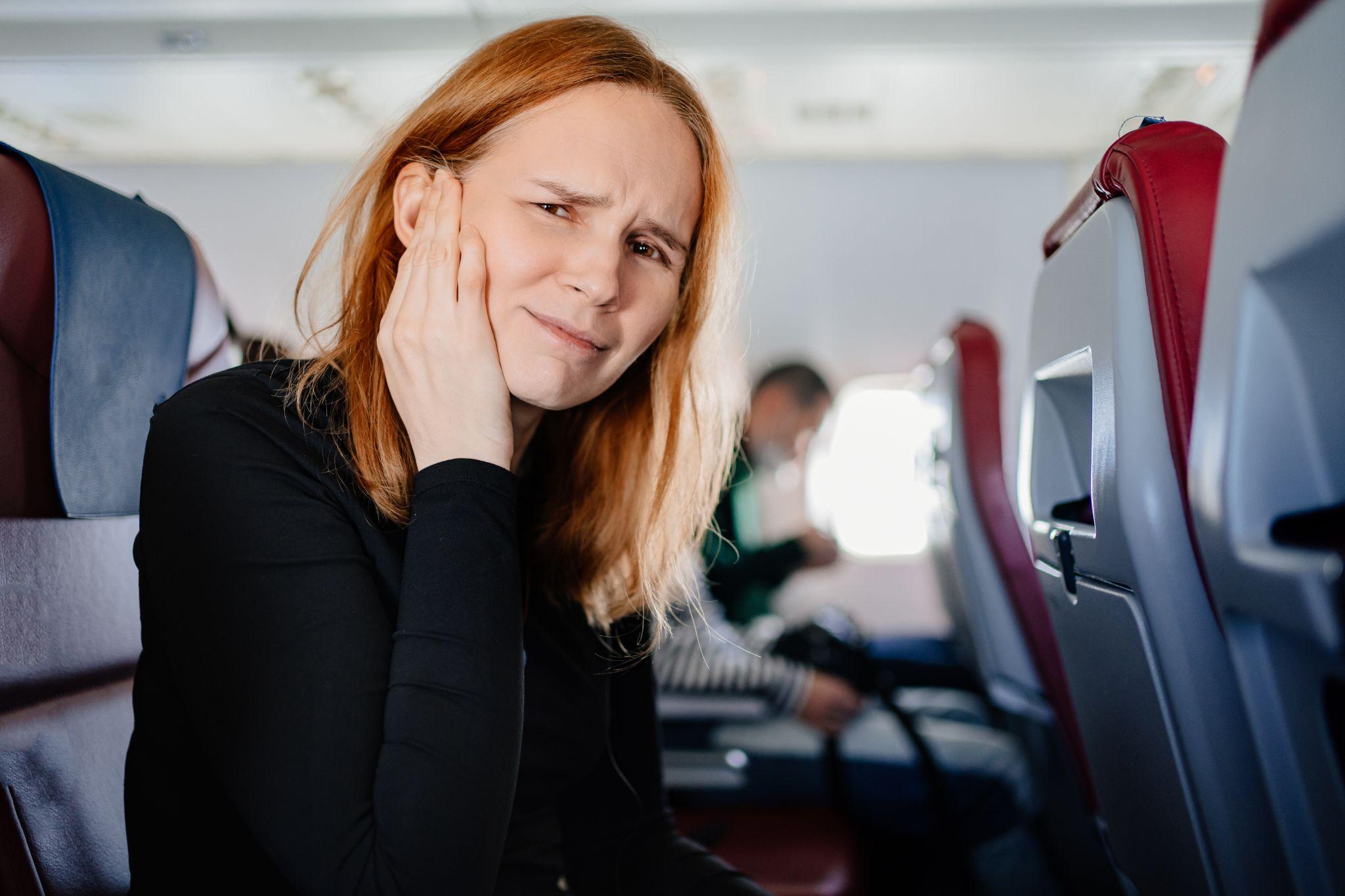 A woman holding her ear in pain while on an airplane