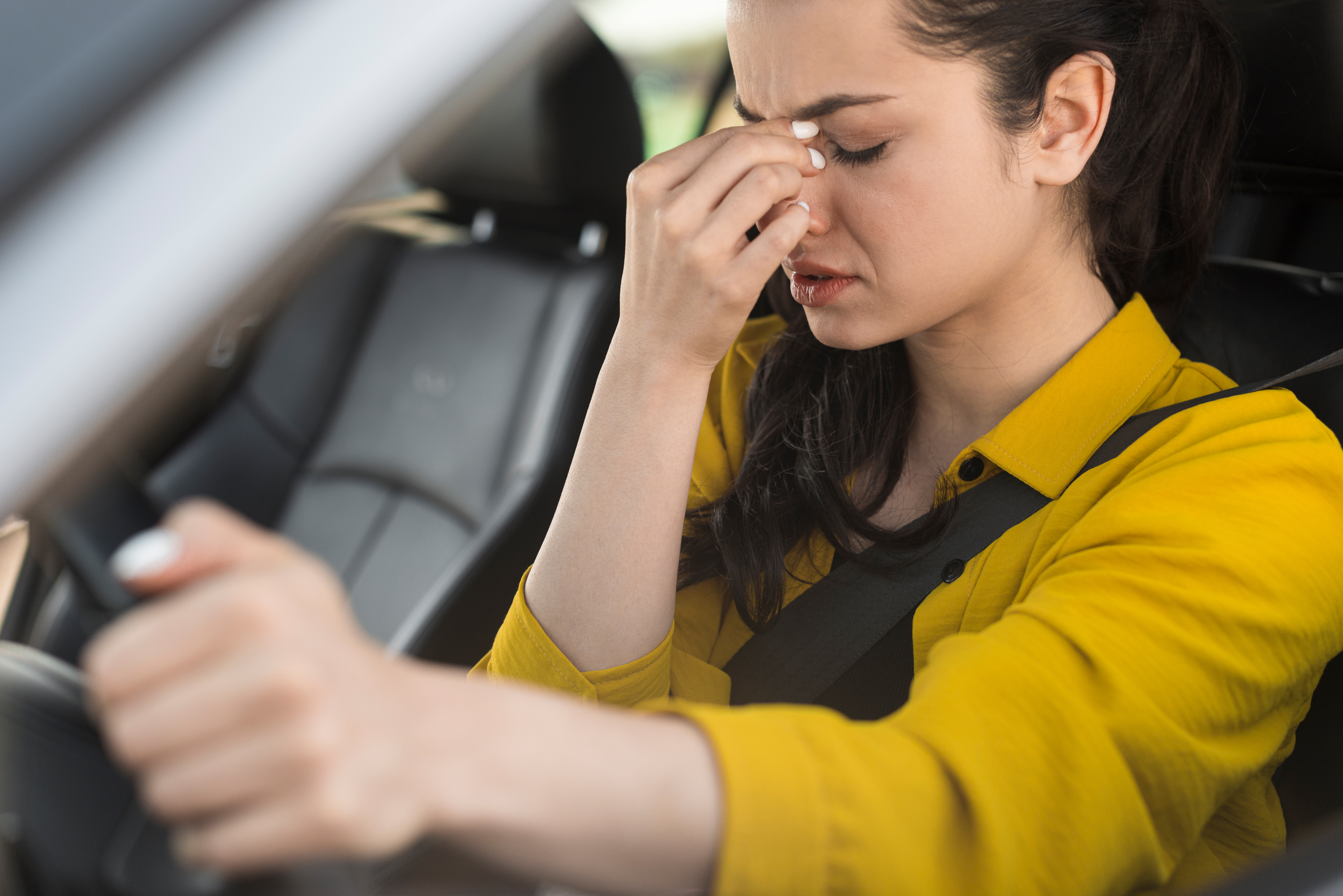 A woman behind the wheel of a car punching her nose in discomfort